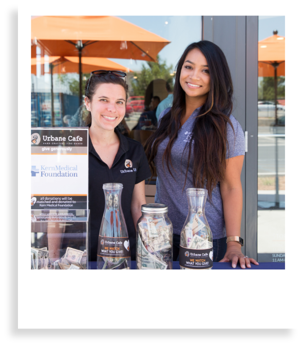 two women standing in front of urbane cafe smiling with jars full of raised money
