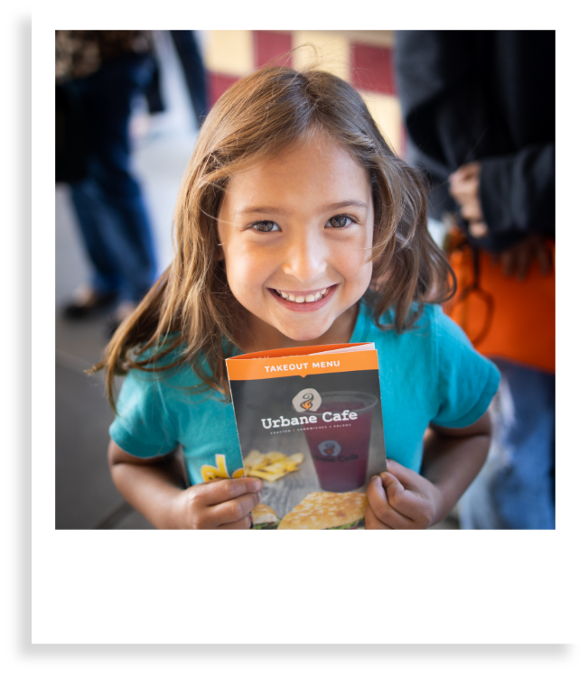 little girl smiling holding urbane cafe brochure